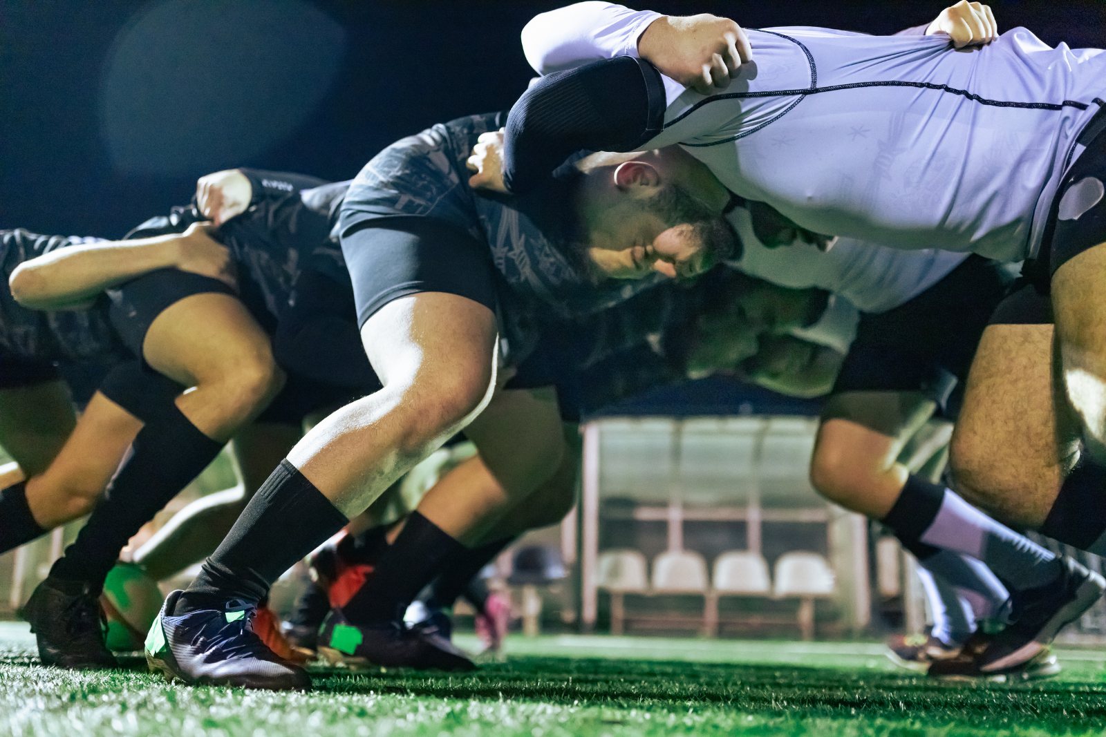 A scrum packing down under floodlights on a wet evening pitch
